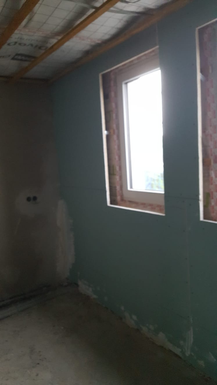 Wnętrze w trakcie montażu płyt kartonowo-gipsowych przy oknie, widoczne szpachlowane łączenia i surowy strop z izolacją.