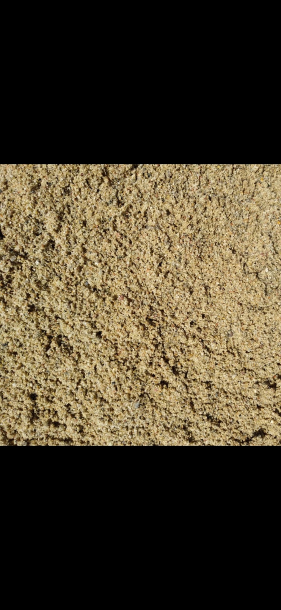 Beżowy, drobnoziarnisty materiał sypki, przypominający piasek kwarcowy, z widoczną strukturą i nierównomiernym oświetleniem.