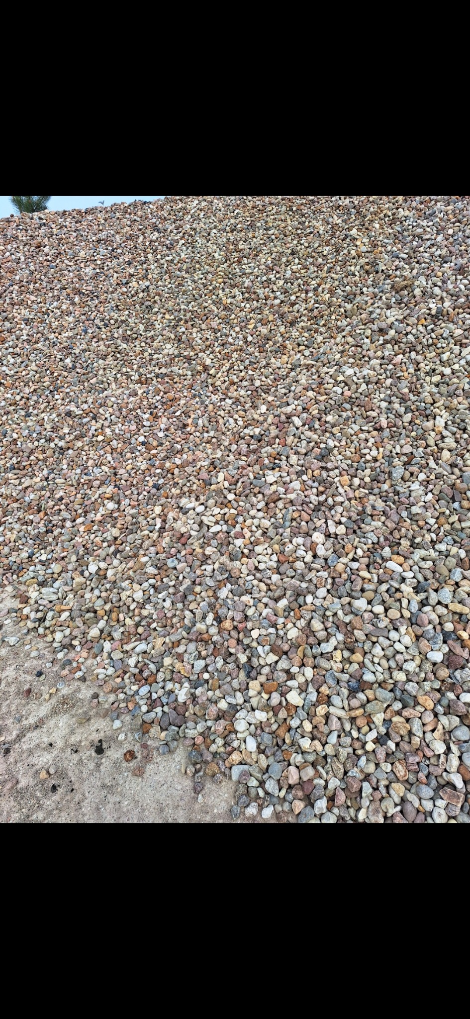 Kopalnia żwiru: Duża pryzma drobnego, kolorowego żwiru z widoczną teksturą i zróżnicowaniem barw, leżąca na ziemi. Widok z bliska, ukazujący różnorodność kształtów i odcieni kamieni.