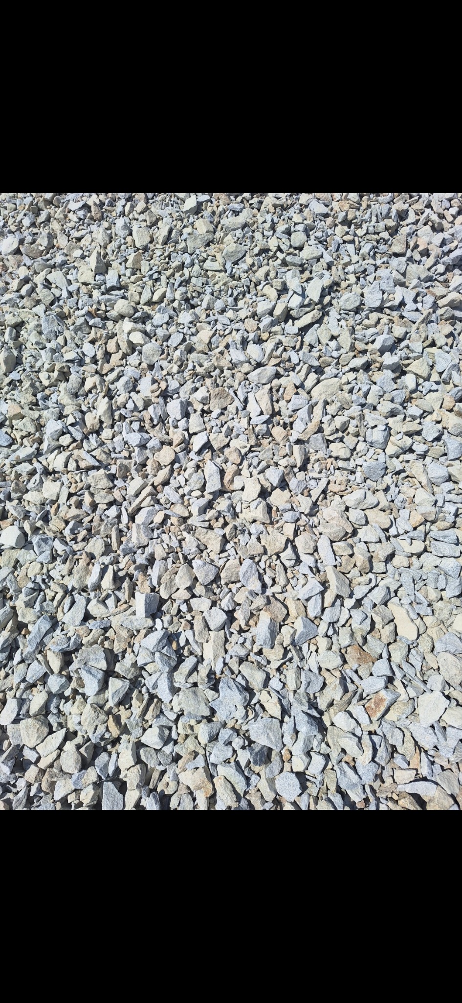 Drobne, szaro-beżowe kamienie tworzące równą powierzchnię, oświetlone jasnym, naturalnym światłem.