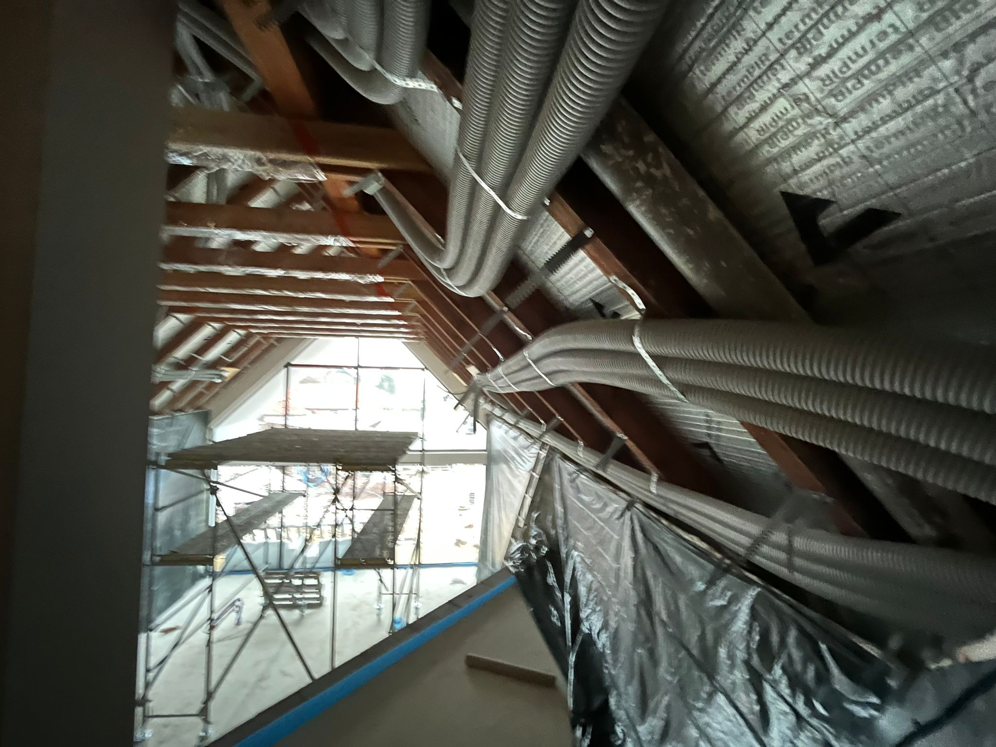 Montaż instalacji rekuperacji na poddaszu, widoczne rury wentylacyjne przymocowane do drewnianej konstrukcji dachu, rusztowanie w tle.