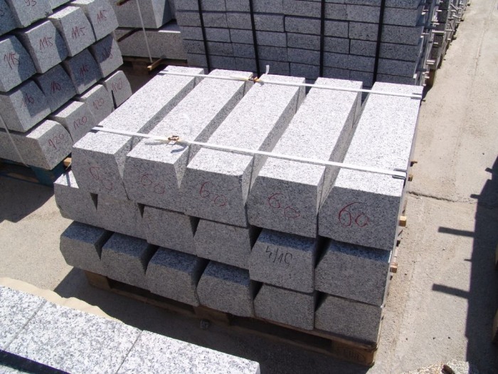 Paleta z jasnoszarymi, granitowymi krawężnikami/opornikami, zabezpieczonymi białymi taśmami, z naniesionymi czerwonymi oznaczeniami wymiarów.