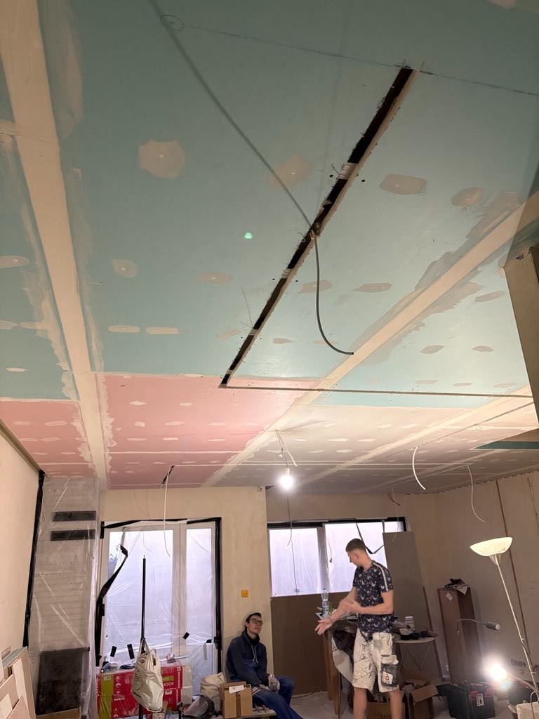 Sufit w trakcie montażu płyt karton-gips, widoczne łączenia i otwór na oświetlenie, dwóch mężczyzn w pomieszczeniu.
