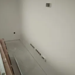 Świeżo wywiercone otwory w ścianie, przygotowane do montażu punktów oświetleniowych, widoczne kartony z elementami wyposażenia i poziomica.