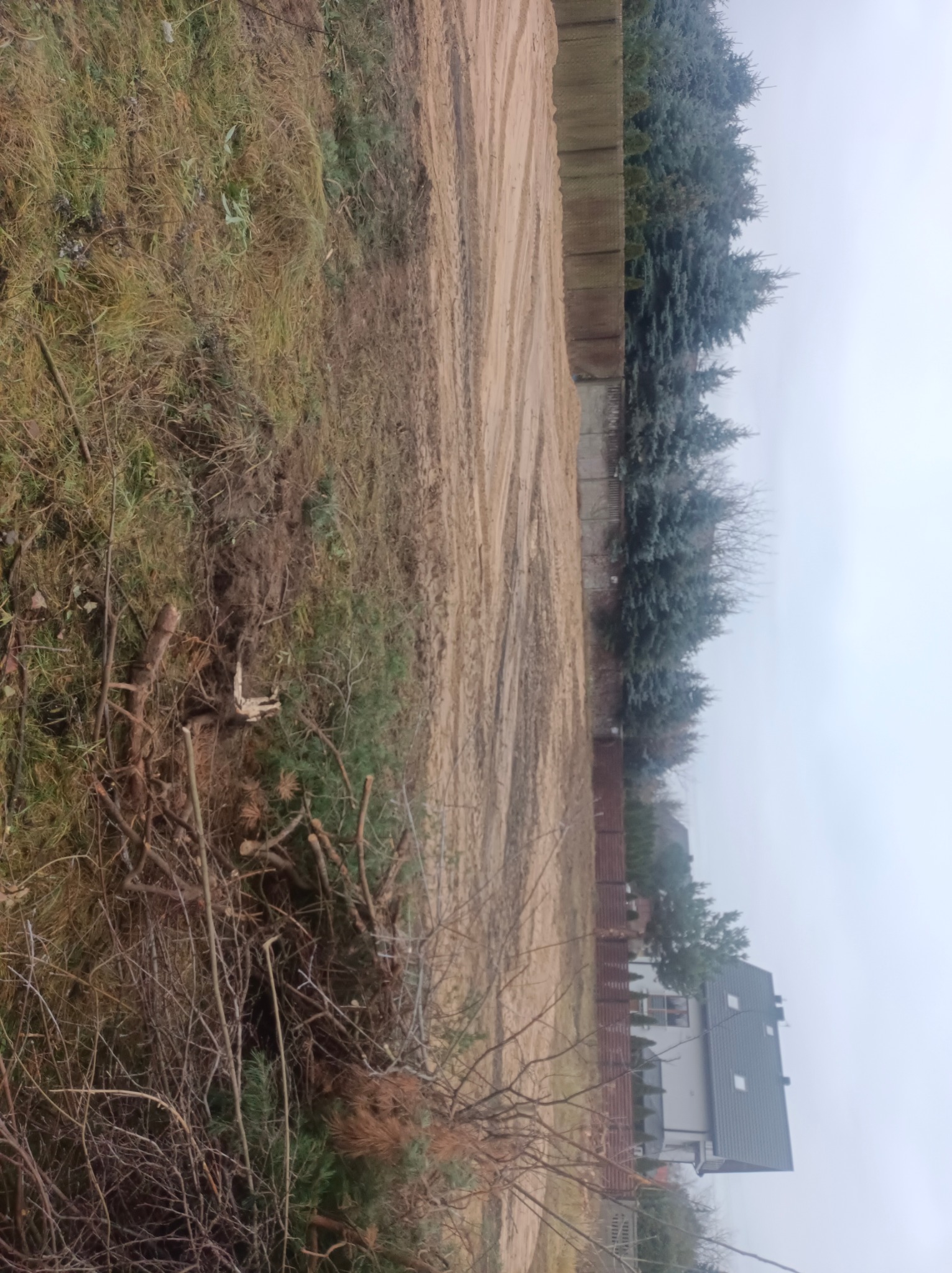 Przygotowany teren pod budowę, widoczne ślady po maszynach, ścięte drzewa i krzewy, ogrodzenie w tle.