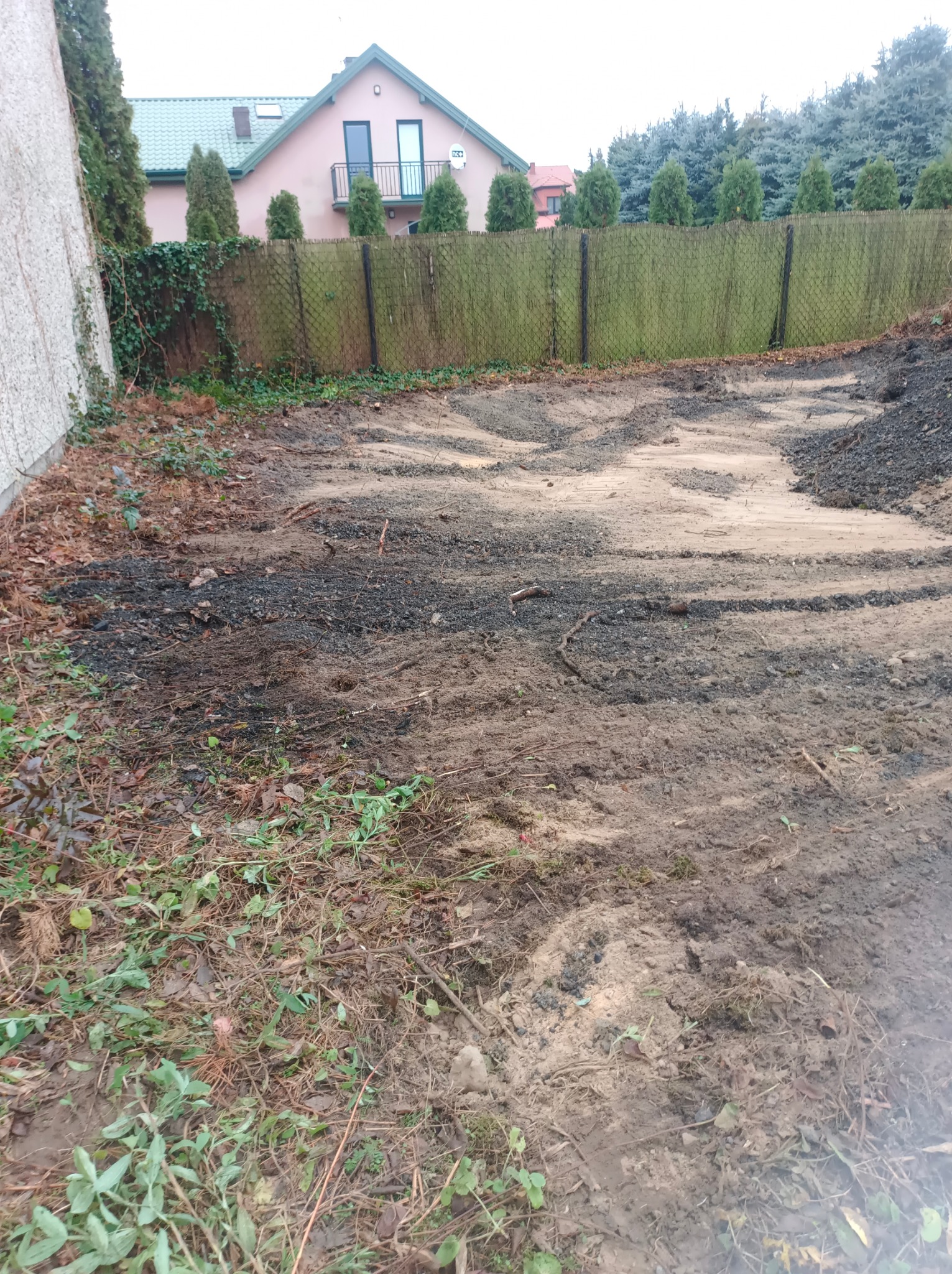 Przygotowany teren pod przyszły ogród, widoczna wyrównana ziemia, resztki roślinności i ogrodzenie z siatki.