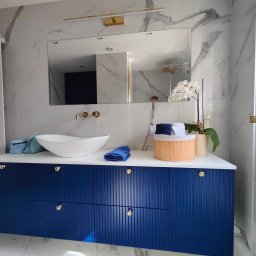 Lamit-Meble Jacek Andrzejczyk - Nowoczesna łazienka z marmurowymi płytkami, umywalką nablatową i szafką w kolorze granatowym z ryflowanymi frontami i złotymi gałkami.