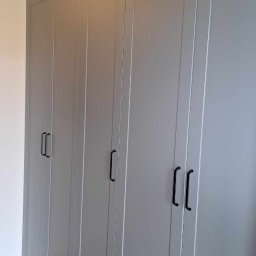 Lamit-Meble Jacek Andrzejczyk - Szara, zabudowana szafa z czarnymi uchwytami, dopasowana do podłogi z paneli w jodełkę. Górne szafki sięgają sufitu. Minimalistyczny design.