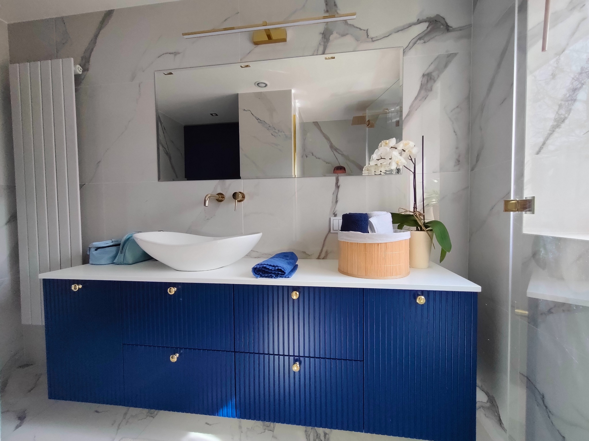 Nowoczesna łazienka z marmurowymi płytkami, umywalką nablatową i szafką w kolorze granatowym z ryflowanymi frontami i złotymi gałkami.