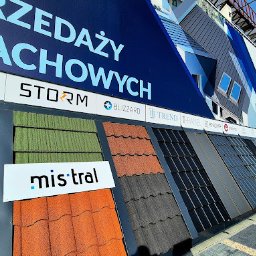 EK-BUD II sp z o.o. - Ekspozycja różnorodnych dachówek w punkcie sprzedaży, z widocznymi markami i modelami. Kolorowe próbki dachówkowe prezentowane na tle reklamowym.