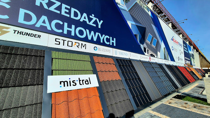 Ekspozycja różnorodnych dachówek w punkcie sprzedaży, z widocznymi markami i modelami. Kolorowe próbki dachówkowe prezentowane na tle reklamowym.