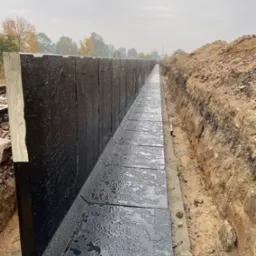 Budowa drenażu liniowego z prefabrykatów betonowych, zabezpieczonych hydroizolacją, w wykopie ziemnym.