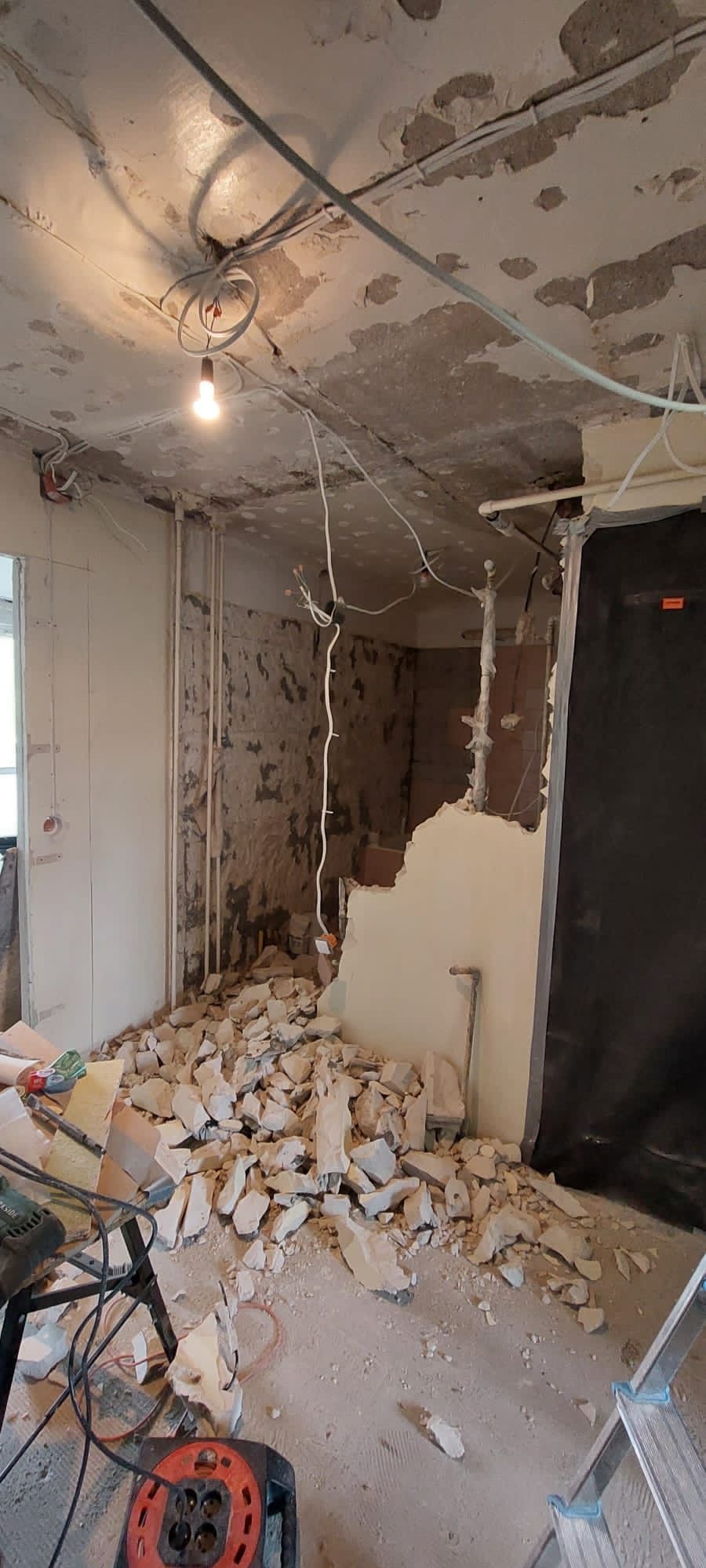 Wnętrze w trakcie demontażu ścian: gruz na podłodze, odsłonięte instalacje elektryczne i hydrauliczne, widoczne narzędzia pracy.