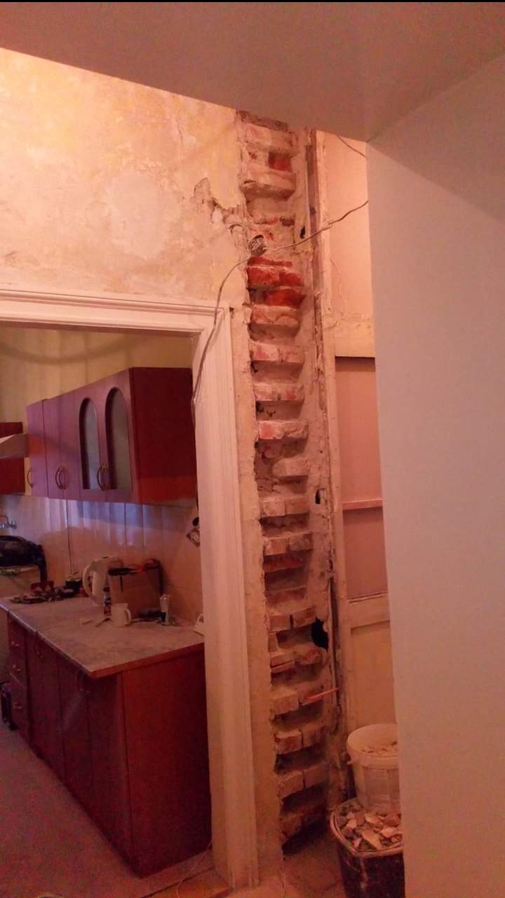 Odsłonięta cegła w trakcie remontu kuchni, widoczne fragmenty instalacji i resztki gruzu. Ściana w trakcie prac przygotowawczych do wykończenia.