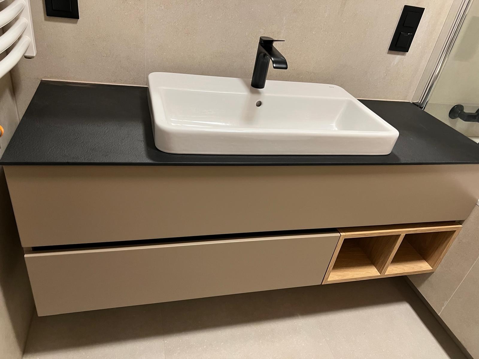 Nowoczesna łazienka: biała umywalka nablatowa z czarną armaturą na beżowej szafce z drewnianymi półkami, czarny blat, jasne płytki. Minimalistyczny design.