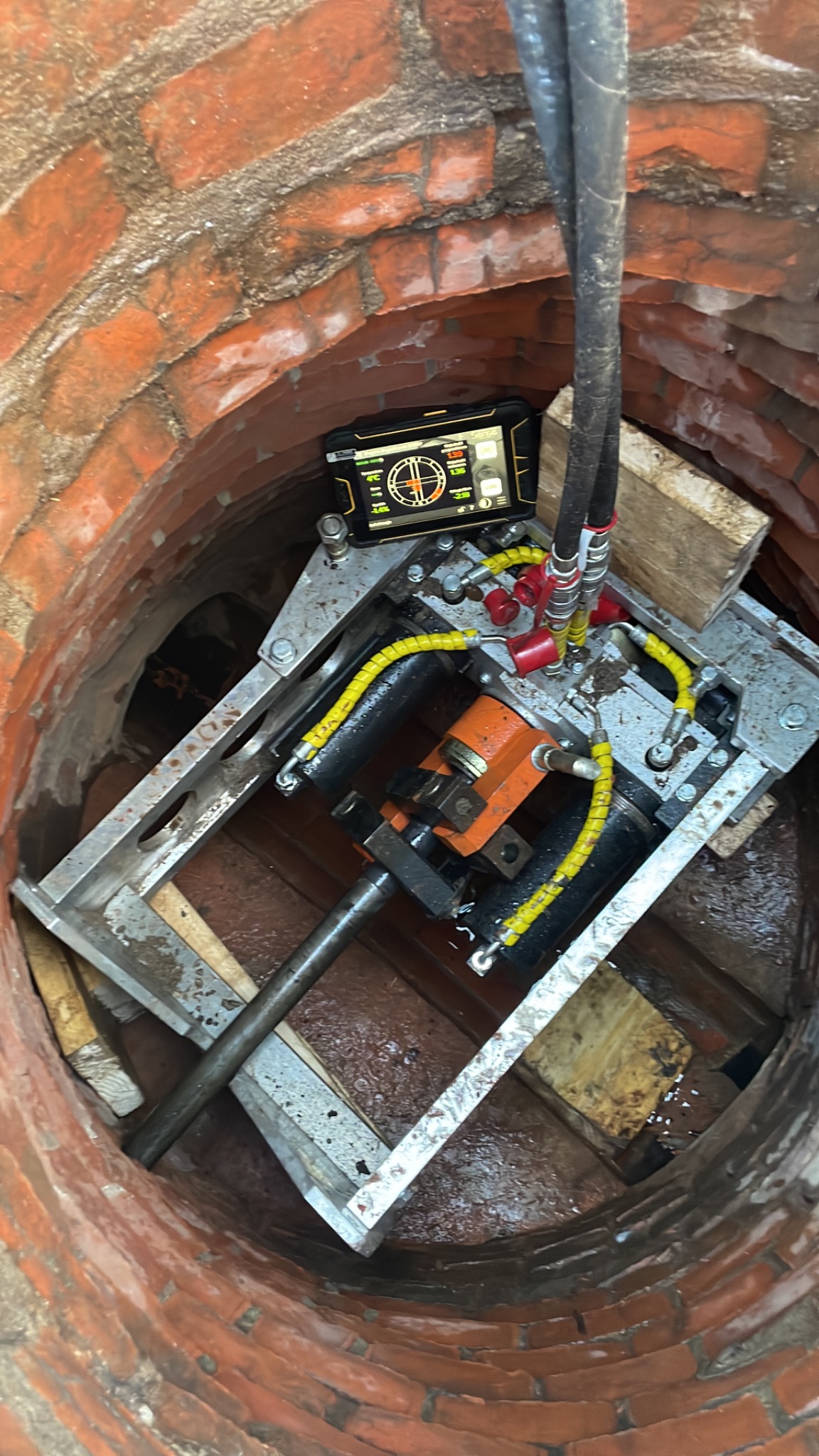Urządzenie do wiercenia kierunkowego w studni z cegły, widoczny ekran sterujący z danymi pomiarowymi.