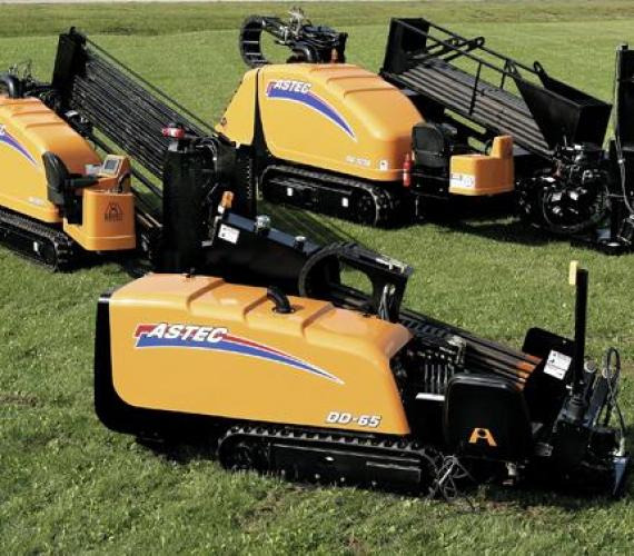 Żółte, gąsienicowe maszyny w trawie, z logo Fastec i oznaczeniem DD-65, na placu budowy.