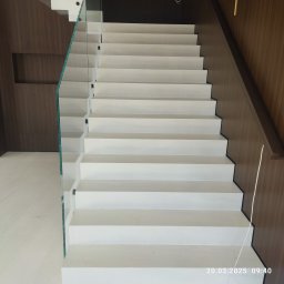 Vasyl Stetsiuk - Nowoczesne, białe schody z szklaną balustradą i drewnianą okładziną ścienną. Minimalistyczny design, jasne oświetlenie, widok od dołu ku górze.