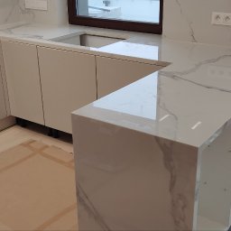 Vasyl Stetsiuk - Nowoczesna, jasna kuchnia z marmurowym blatem i białymi szafkami, widok z góry, zabezpieczona podłoga kartonem, okno w tle.