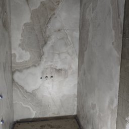 Vasyl Stetsiuk - Wnętrze łazienki w trakcie prac. Położone płytki imitujące marmur na ścianach, widoczne kable pod sufitem, częściowo ułożona podłoga.