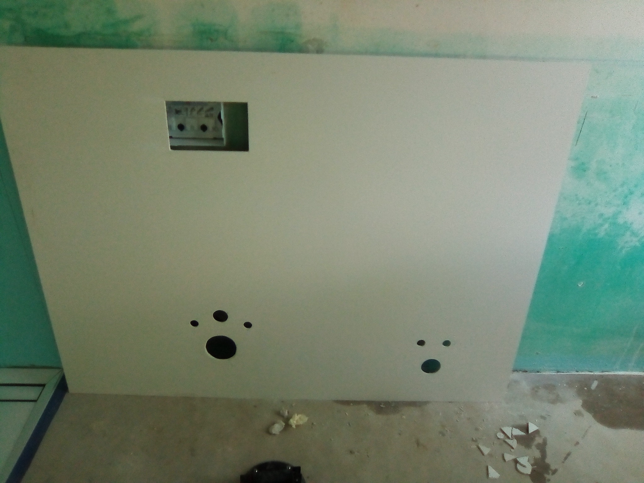 Płyta gipsowa z wyciętymi otworami na instalacje elektryczne i hydrauliczne, przytwierdzona do ściany w trakcie prac wykończeniowych w łazience.