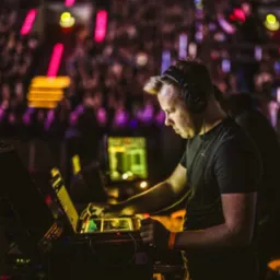 DJ w słuchawkach miksuje muzykę na laptopie z kontrolerem, w tle rozświetlony tłum.