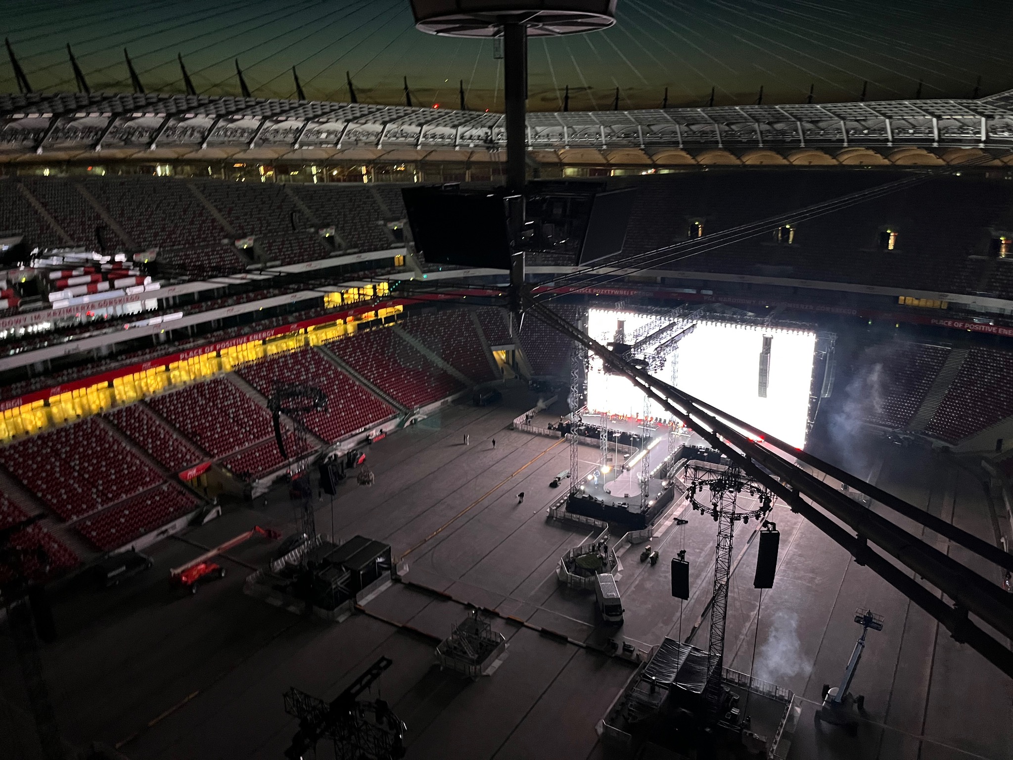 Przygotowania do koncertu na stadionie: widok z góry na scenę, nagłośnienie i oświetlenie w trakcie montażu, z widocznymi elementami konstrukcyjnymi i pustymi trybunami