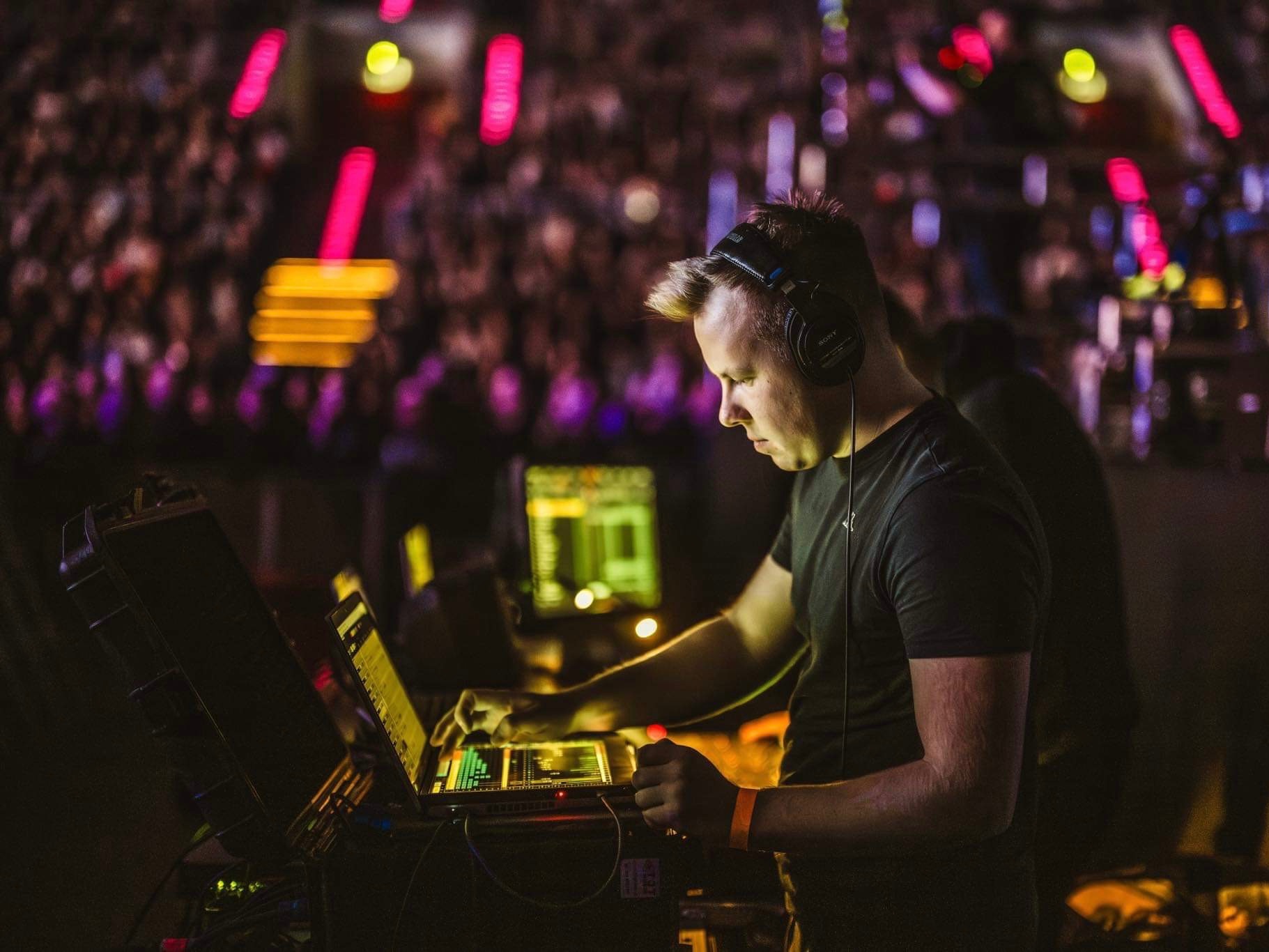 DJ w słuchawkach miksuje muzykę na laptopie z kontrolerem, w tle rozświetlony tłum.