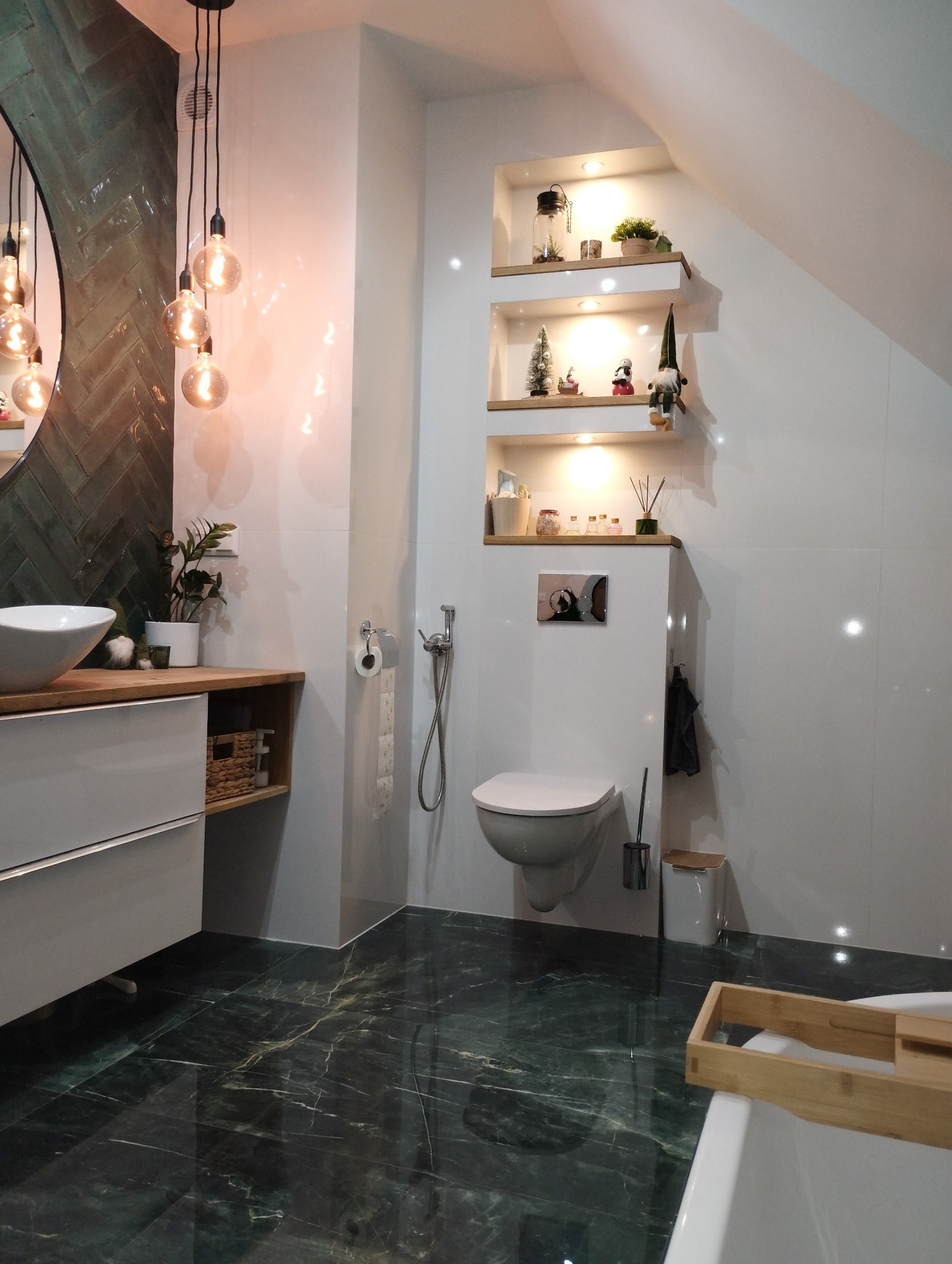 Nowoczesna łazienka z zieloną, marmurkową podłogą, białymi płytkami na ścianach, podwieszaną toaletą, umywalką nablatową i dekoracyjnymi półkami w ścianie.
