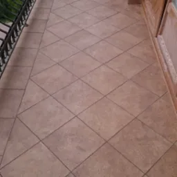 Wykończony balkon w Chełmie z brązowymi płytkami ułożonymi w romby, czarna, ozdobna balustrada i drewniane drzwi balkonowe.