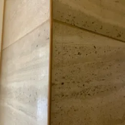 Szczegółowe ujęcie narożnika wykończonego trawertynem z widocznymi żyłami i fugą w odcieniach beżu.