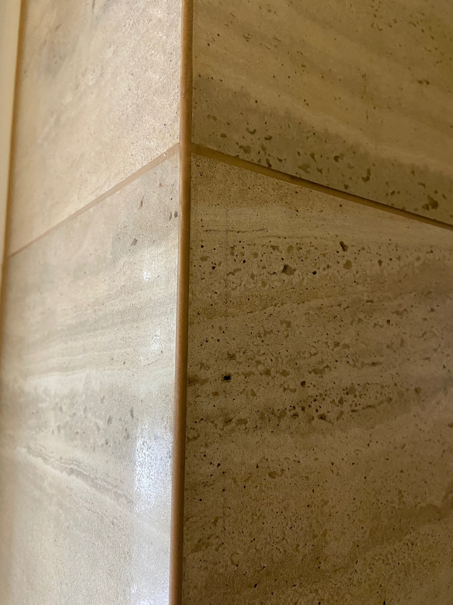 Szczegółowe ujęcie narożnika wykończonego trawertynem z widocznymi żyłami i fugą w odcieniach beżu.