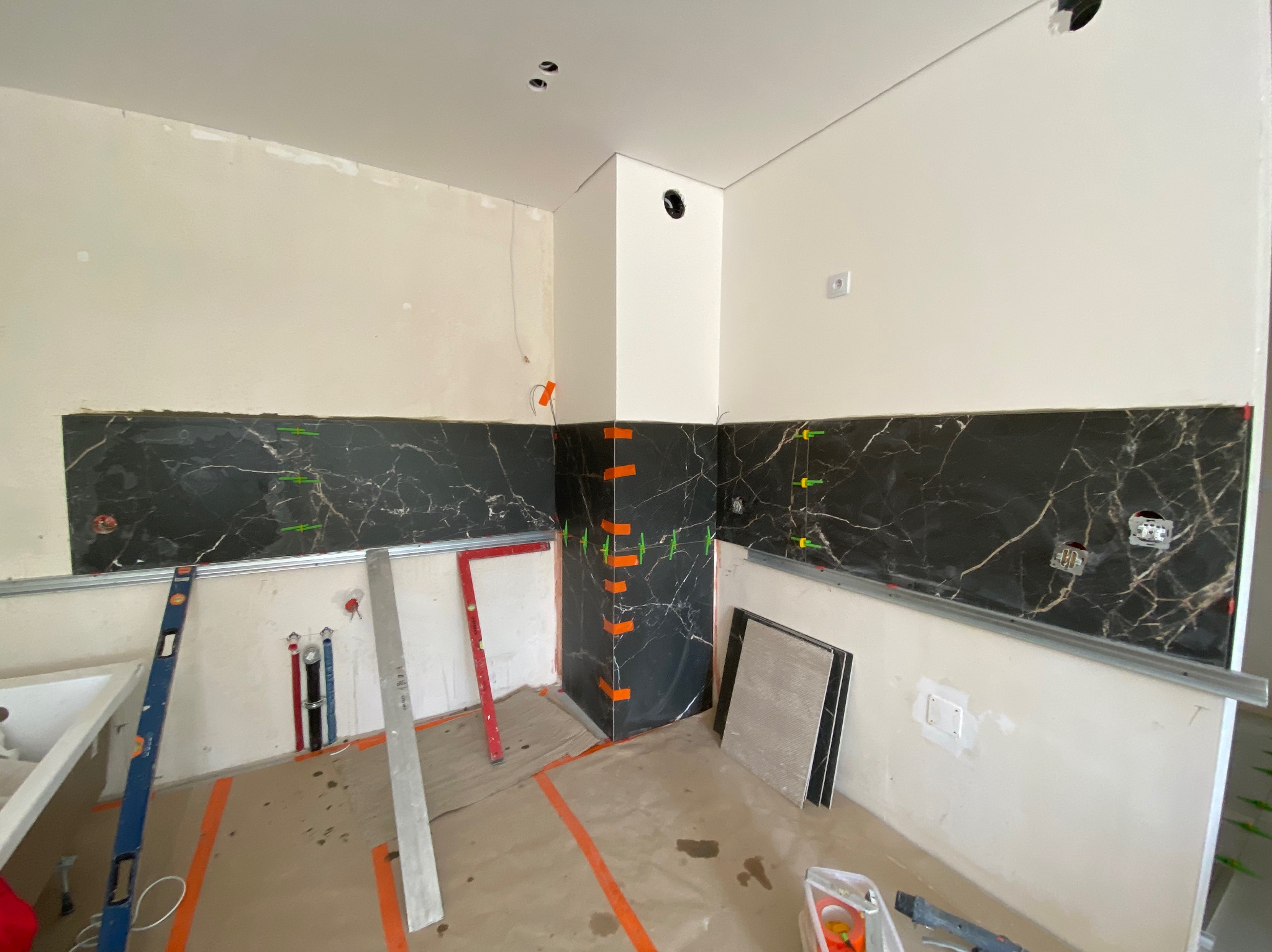 Montaż czarnych płytek imitujących marmur na ścianie w trakcie remontu łazienki, widoczne poziomice, listwy montażowe i krzyżyki dystansowe.
