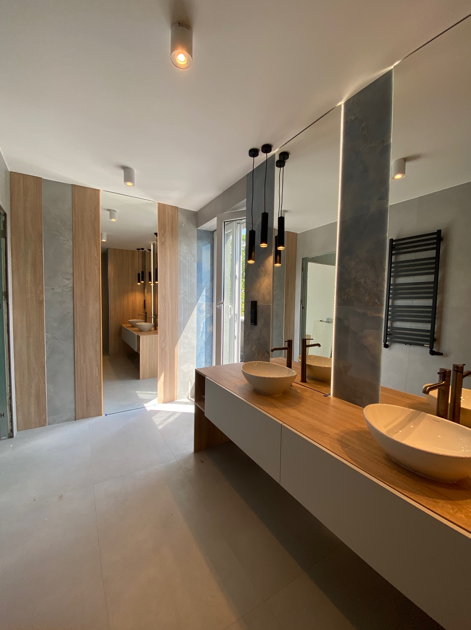 Nowoczesna łazienka z podwójną umywalką nablatową, drewnianym blatem i panelami ściennymi w odcieniach szarości i drewna. Oświetlenie punktowe i wiszące lampy.