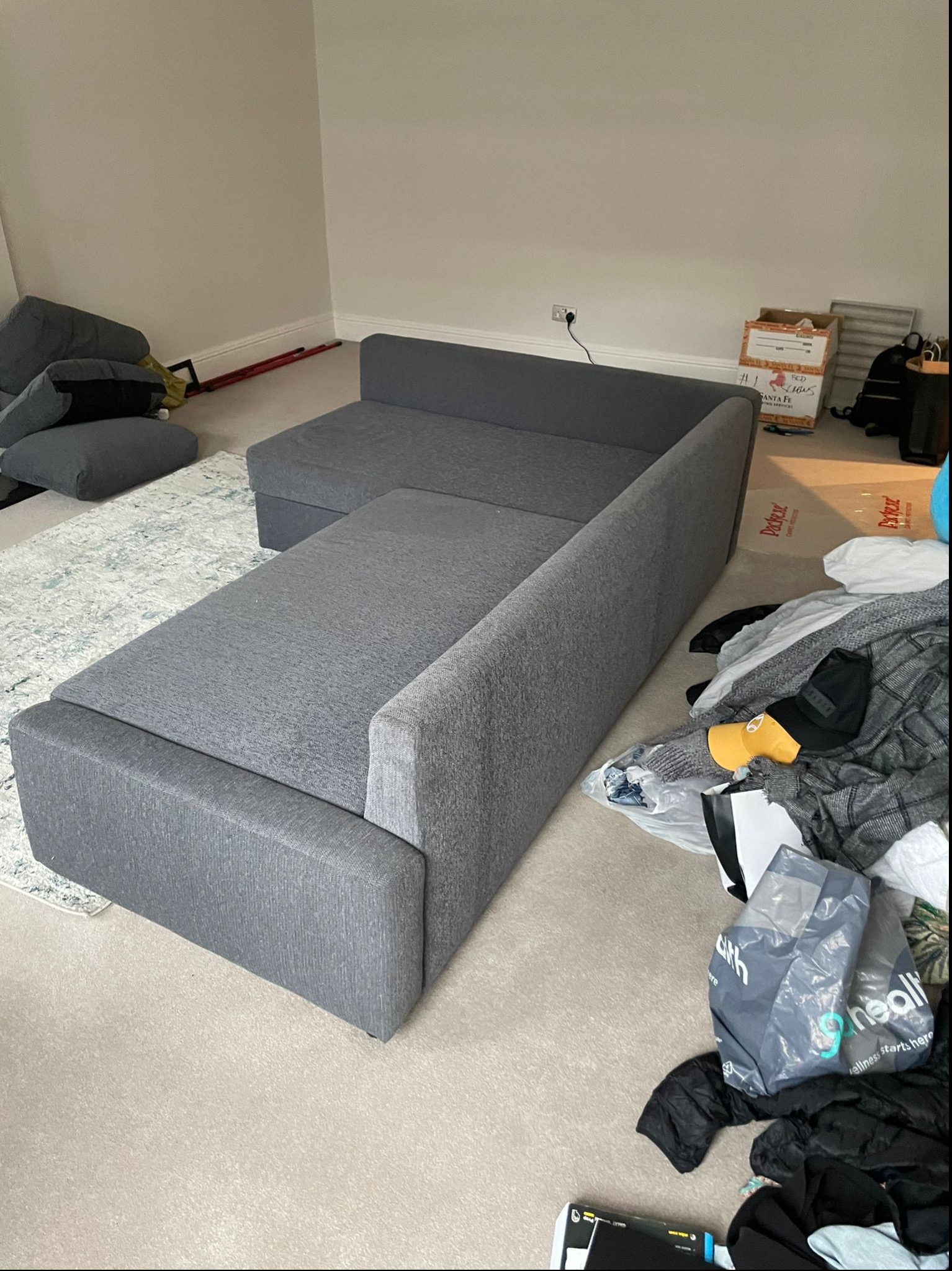 Rozłożona szara sofa modułowa w trakcie montażu, widoczne kartony i rozpakowane elementy na podłodze, dywan w tle.