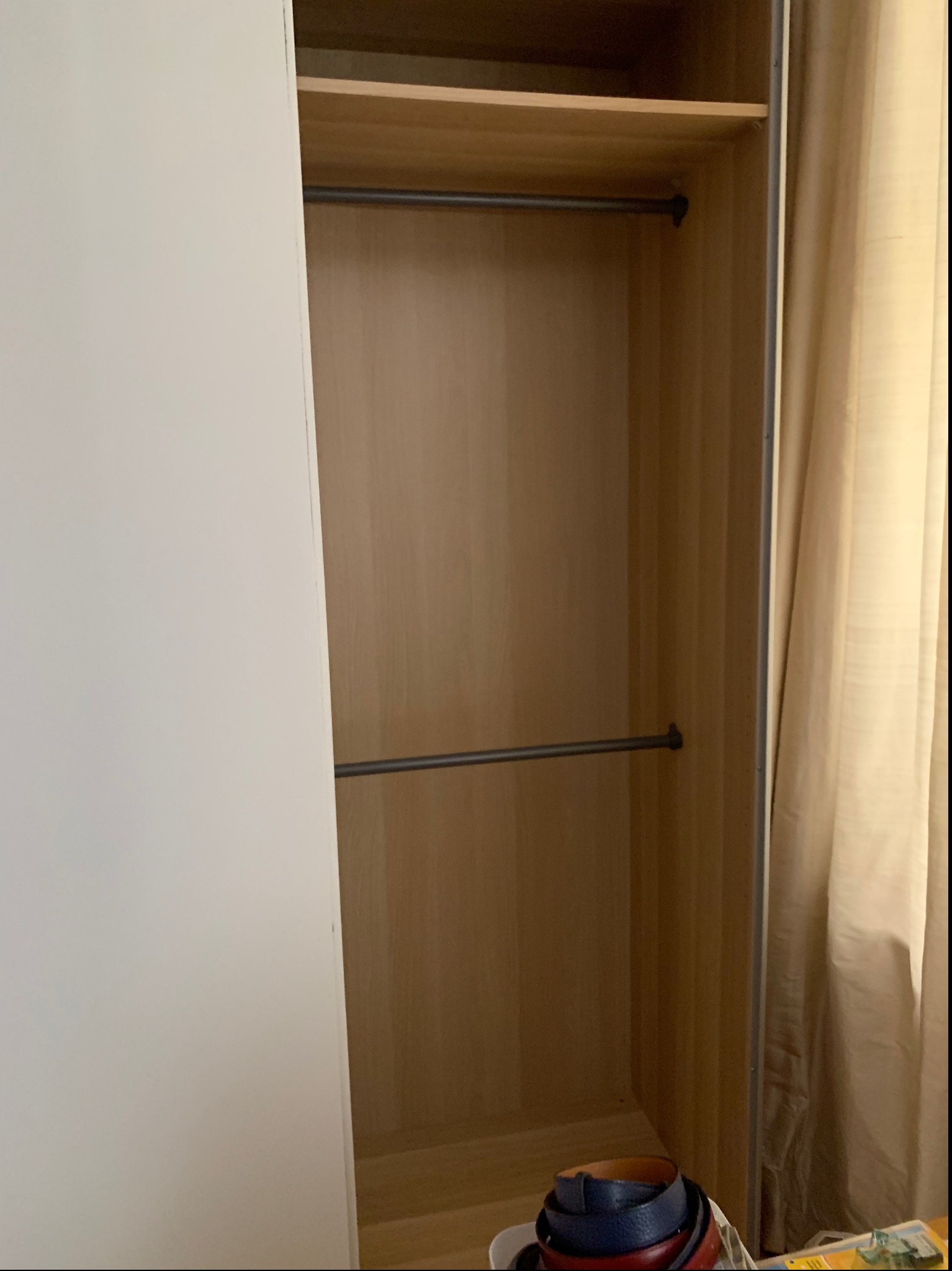 Wnętrze szafy Ikea Pax z dwiema półkami i drążkami na ubrania, widoczne paski na dole, częściowo zasłonięte białymi drzwiami.