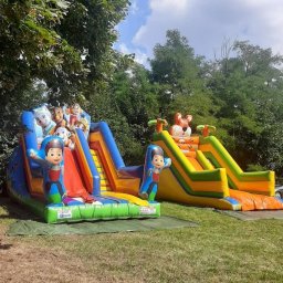 Gres - Dwa kolorowe dmuchane zamki ze zjeżdżalniami na trawie, jeden z motywem Psiego Patrolu, drugi z tygrysem na szczycie.