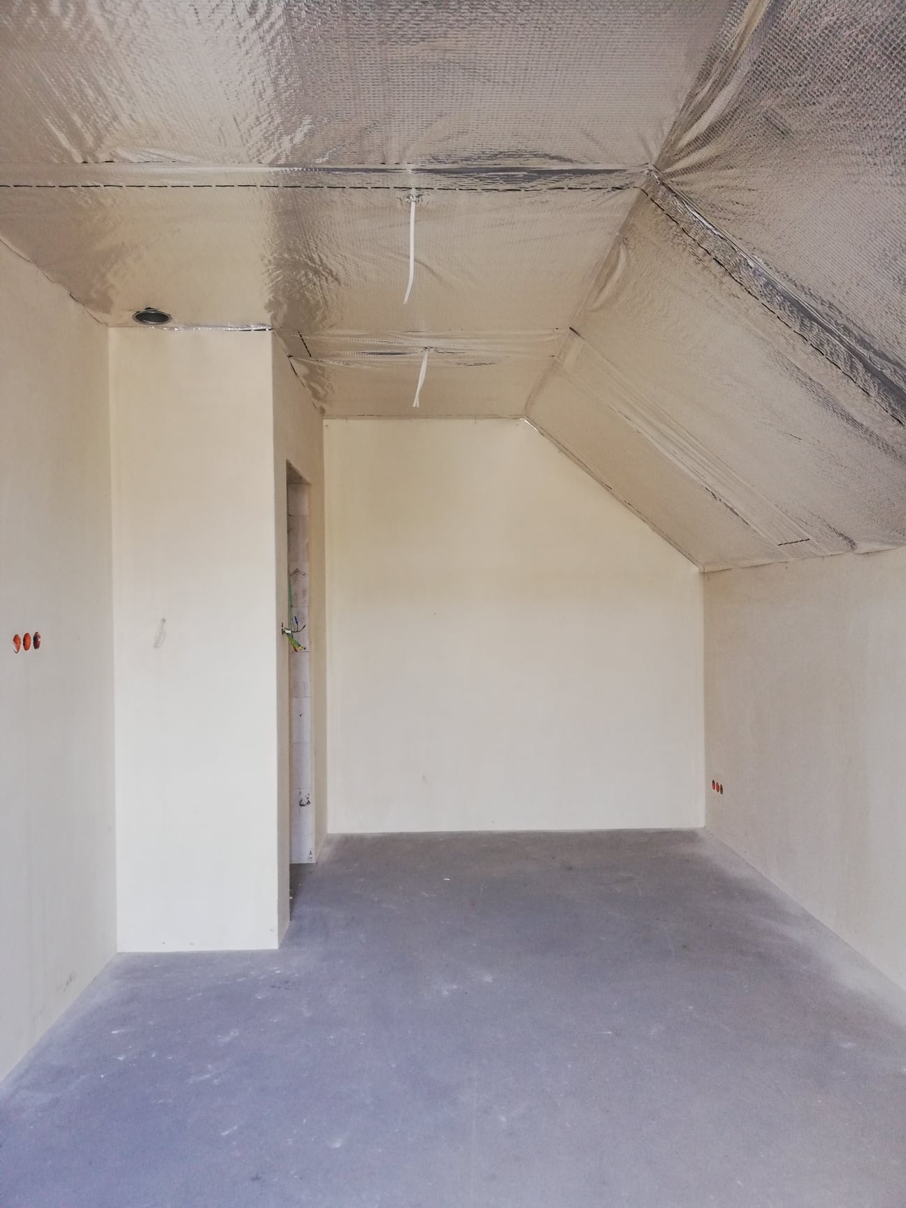 Poddasze po szpachlowaniu i izolacji folią aluminiową, widoczne punkty elektryczne i przygotowane otwory na oświetlenie.