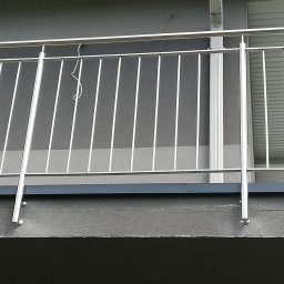 BAR ANDRZEJ ANDRZBAR - Balkon z nowoczesną, minimalistyczną balustradą ze stali nierdzewnej, widok z dołu, szary tynk strukturalny budynku w tle.