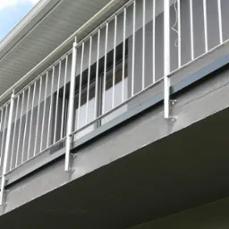 Balkon z nowoczesną, minimalistyczną balustradą ze stali, widok z dołu, z widocznymi mocowaniami do betonowej konstrukcji balkonu, na jednej z pionowych rurek wisi haczyk.