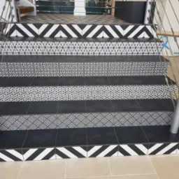 Schody wyłożone czarno-białą, wzorzystą glazurą, z metalową barierką. Widoczne różne wzory na poszczególnych stopniach. Oryginalne wykończenie wnętrza.