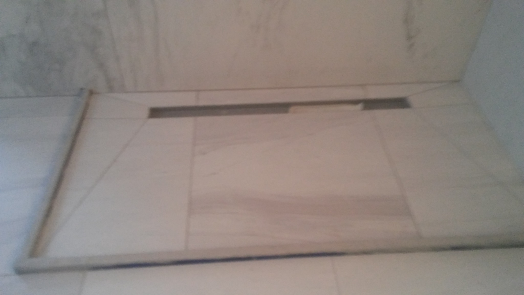 Ukończony brodzik z odpływem liniowym, wyłożony jasnymi płytkami w Pułtusku. Widoczne fugi i delikatny wzór na płytkach.