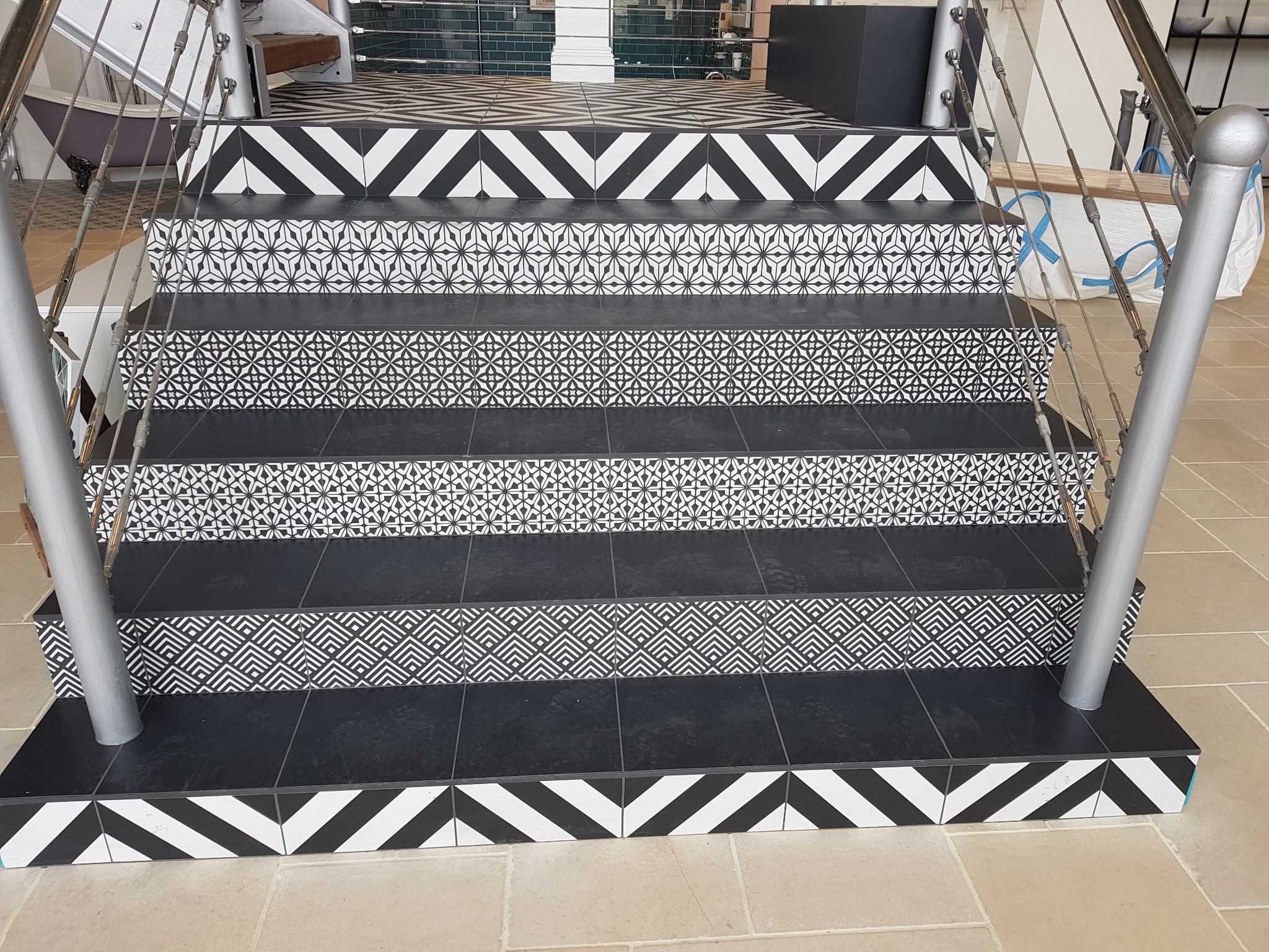 Schody wyłożone czarno-białą, wzorzystą glazurą, z metalową barierką. Widoczne różne wzory na poszczególnych stopniach. Oryginalne wykończenie wnętrza.