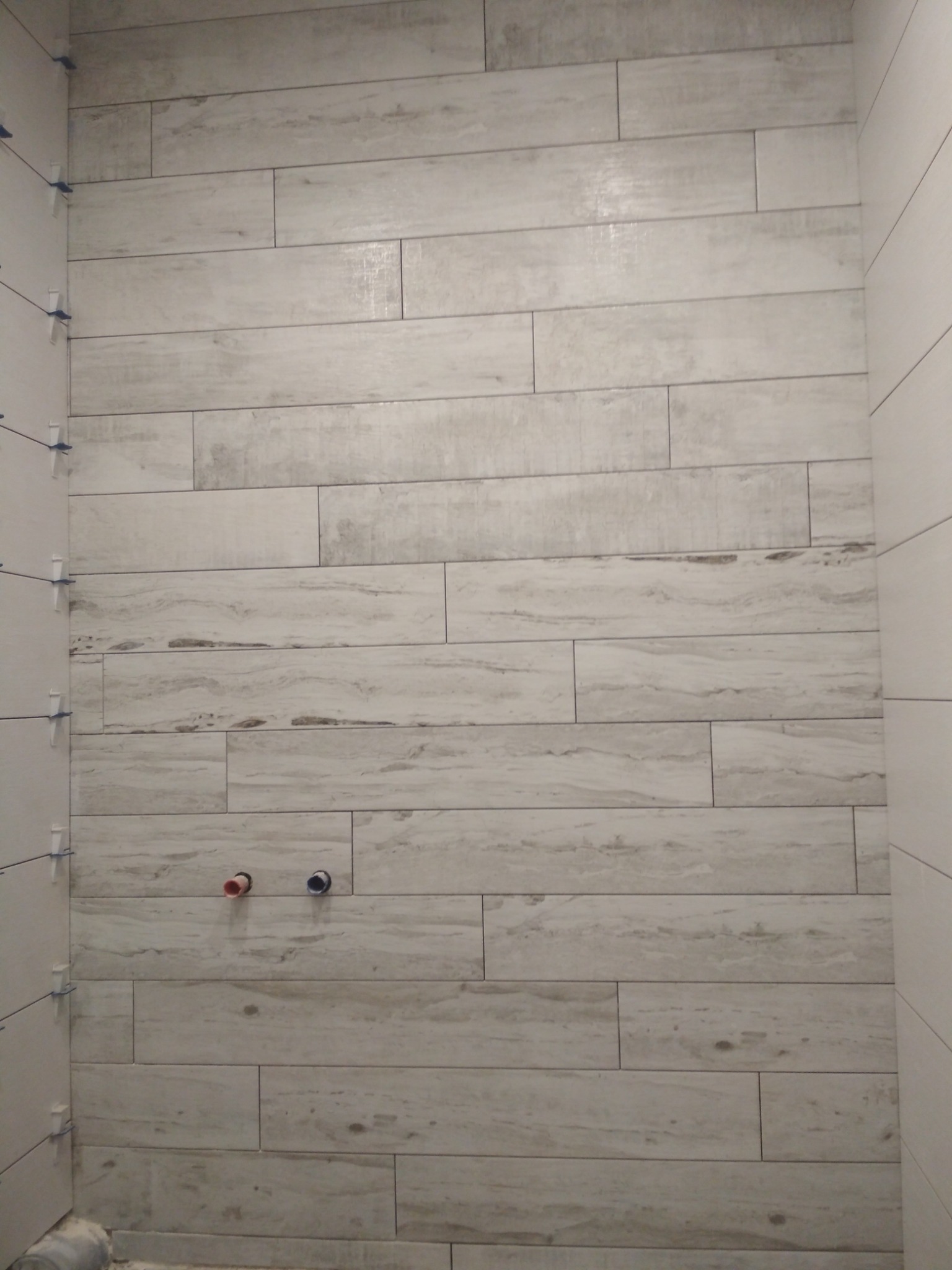 Ściana łazienki w trakcie układania płytek imitujących drewno, widoczne krzyżyki dystansowe, wyprowadzenia instalacji wodnej.