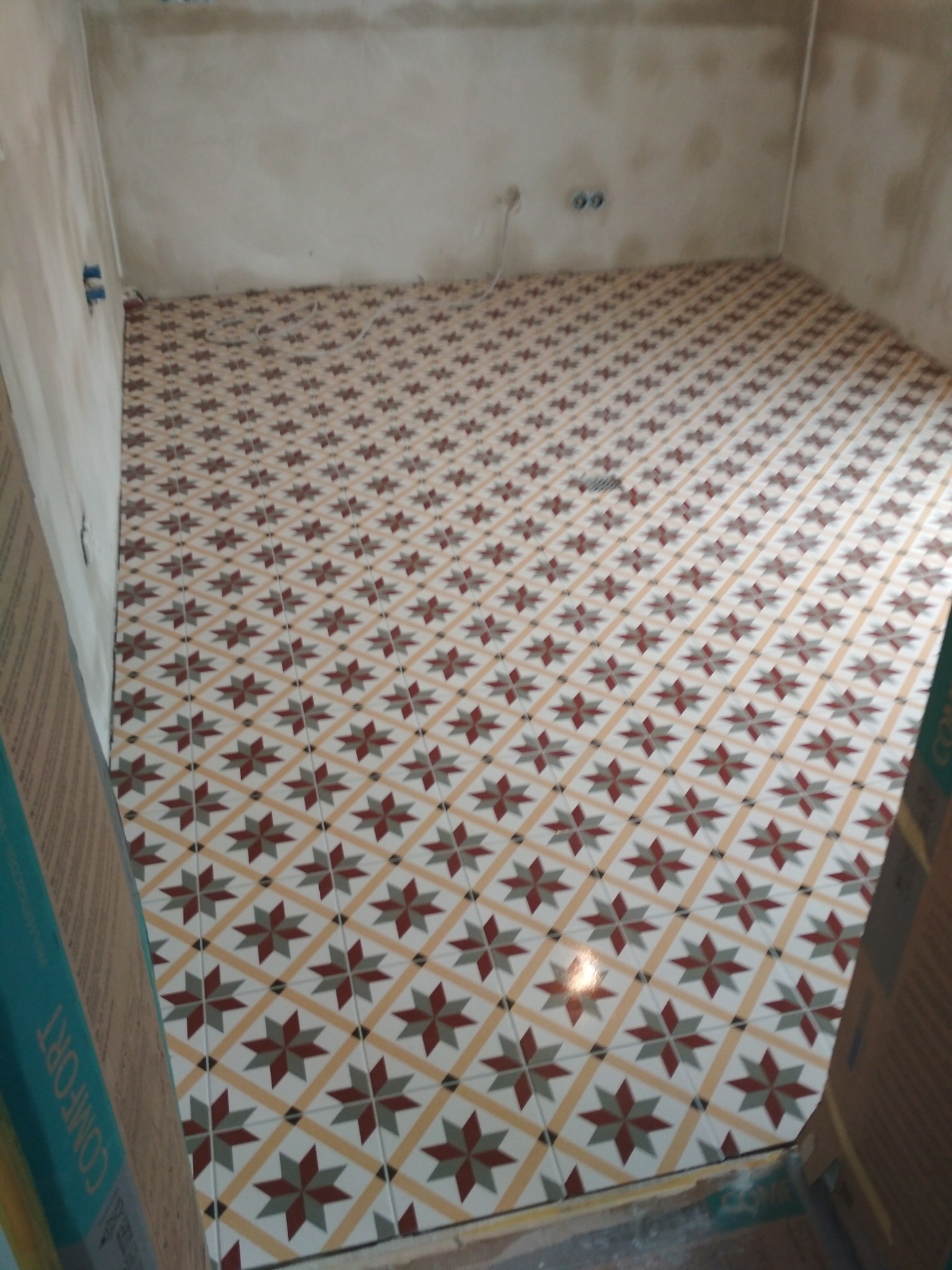 Ukończona podłoga w pomieszczeniu z wzorem w gwiazdy, widoczne surowe ściany i kartony płytek po bokach.