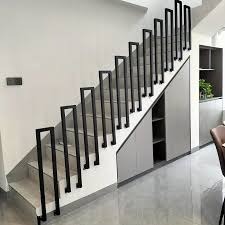 Minimalistyczne schody z czarną, pionową balustradą i szarymi szafkami pod biegiem, oświetlone naturalnym światłem. Nowoczesny design, delikatne detale wykończenia.