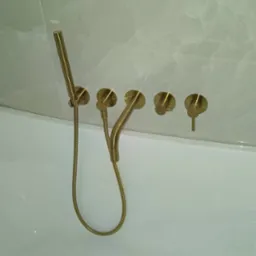 Złota bateria wannowa ścienna z deszczownicą i czterema pokrętłami, zamontowana nad białą wanną z widoczną etykietą producenta Cersanit.