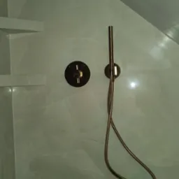 Nowoczesna kabina prysznicowa z marmurowymi płytkami, wyposażona w złotą baterię termostatyczną i słuchawkę prysznicową na wężu, zamontowaną na ścianie.