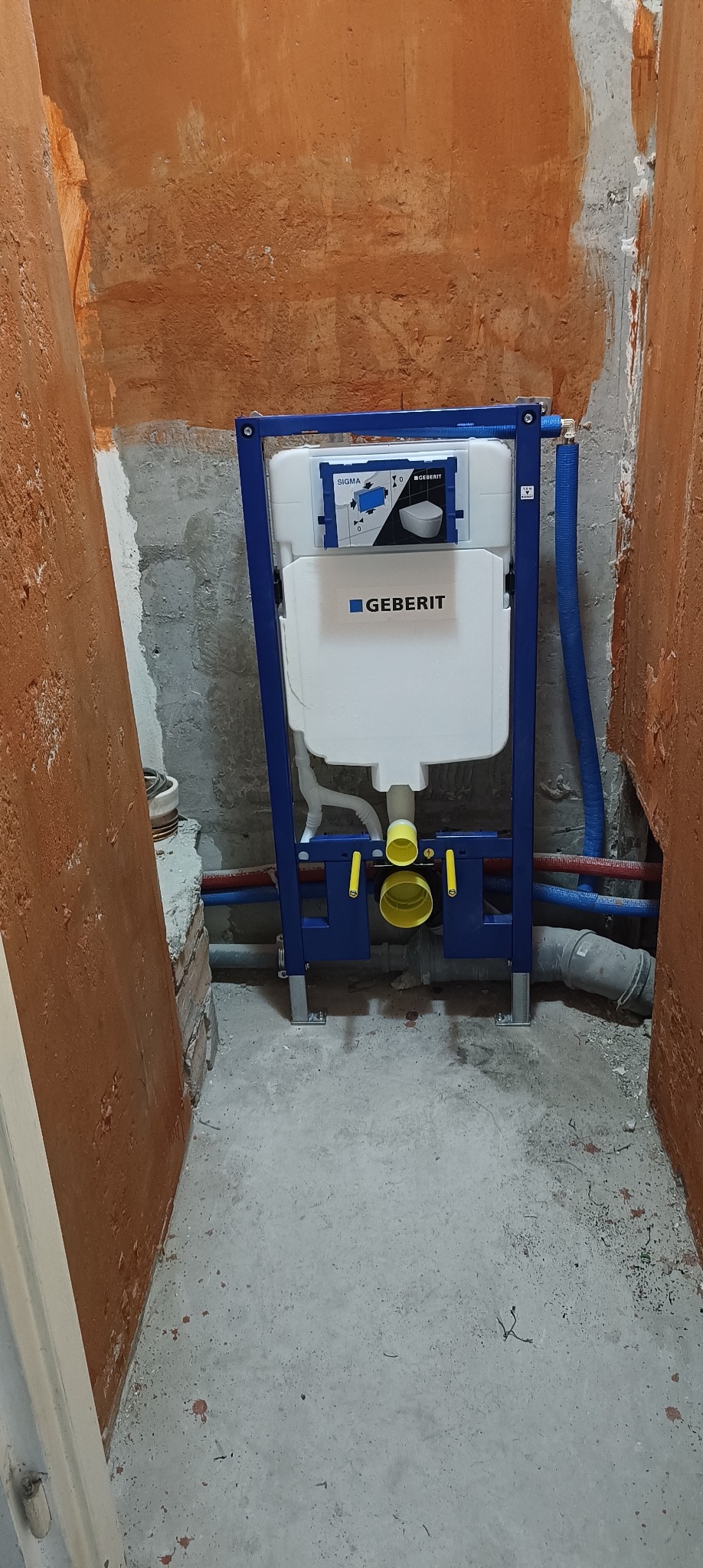 Stelaż podtynkowy Geberit Sigma zamontowany w surowej łazience z widocznymi rurami instalacyjnymi, przed zabudową.