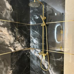 ADEOBUD - Elegancka kabina prysznicowa z czarnymi płytkami imitującymi marmur, złotą armaturą i podświetlanym lustrem. Nowoczesny design łazienki.